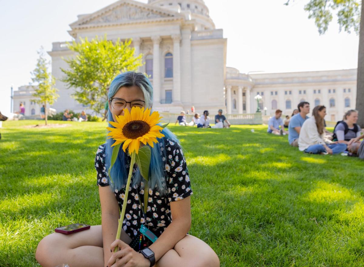 A person holds a sunflower in front of the Capitol Building in Madison, WI
