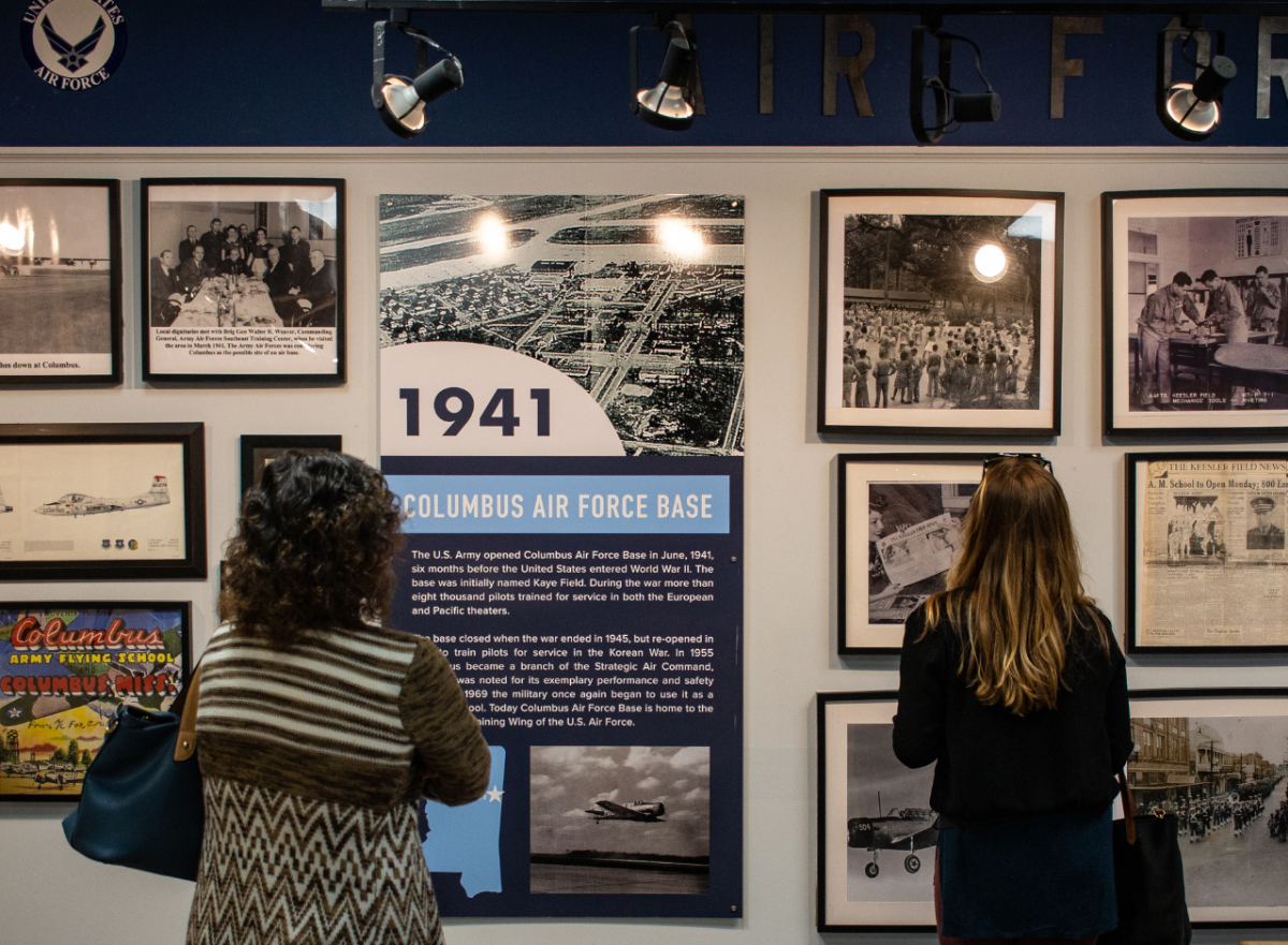Tourists looking at exhibit wall of images and history at Mississippi Aviation Heritage Museum.
