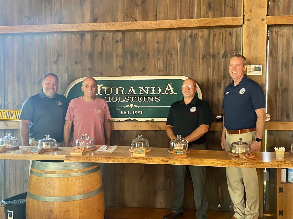 NYS Assemblyman standing with owner of Muranda Cheese in front of the sign inside of a rustic wooden barn