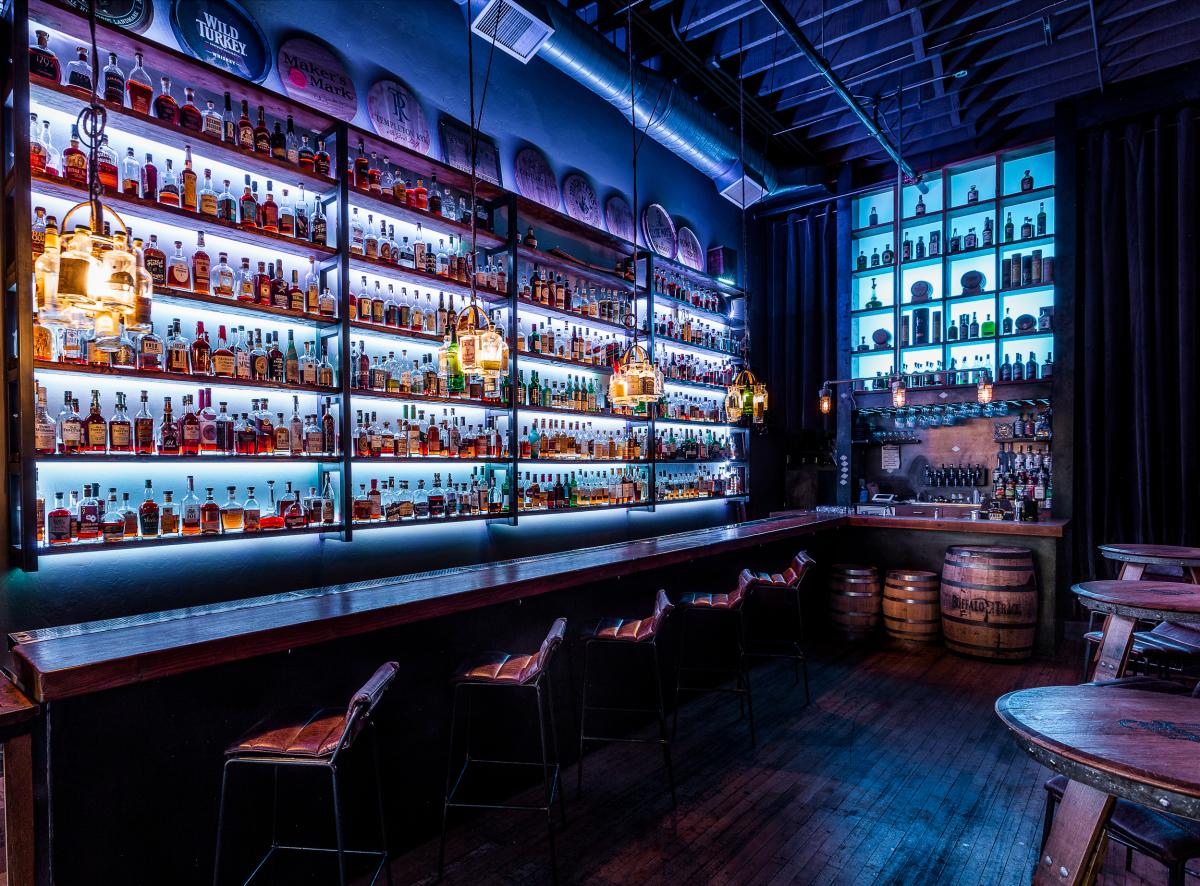 Dim whiskey bar with blue lighting, stools and a bar