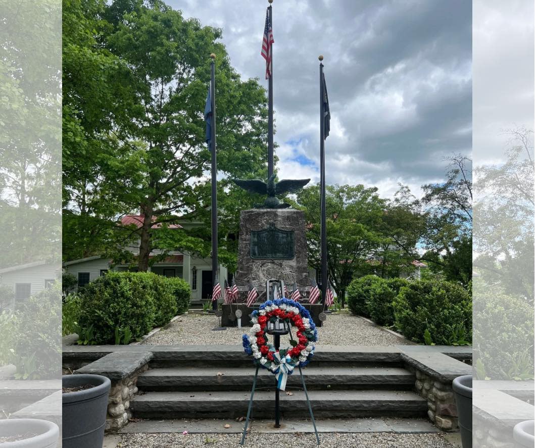 An American flag flying over a monument with flowers at the Pike County America250PA tree planting.