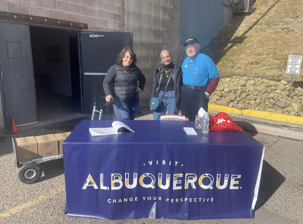 Three people stand behind a Visit Albuquerque table during Partner Pickup for 2024 Visitors Guides