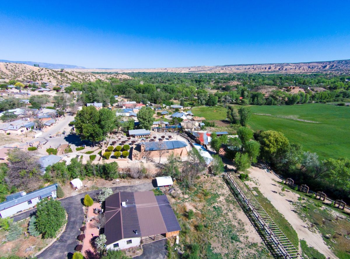 a small town with a variety of buildings sits next to green fields and sparse desert hillsides