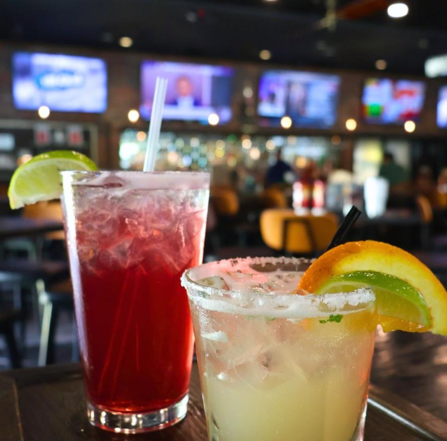 Two Cocktails sitting on a table with four TV screens in the background