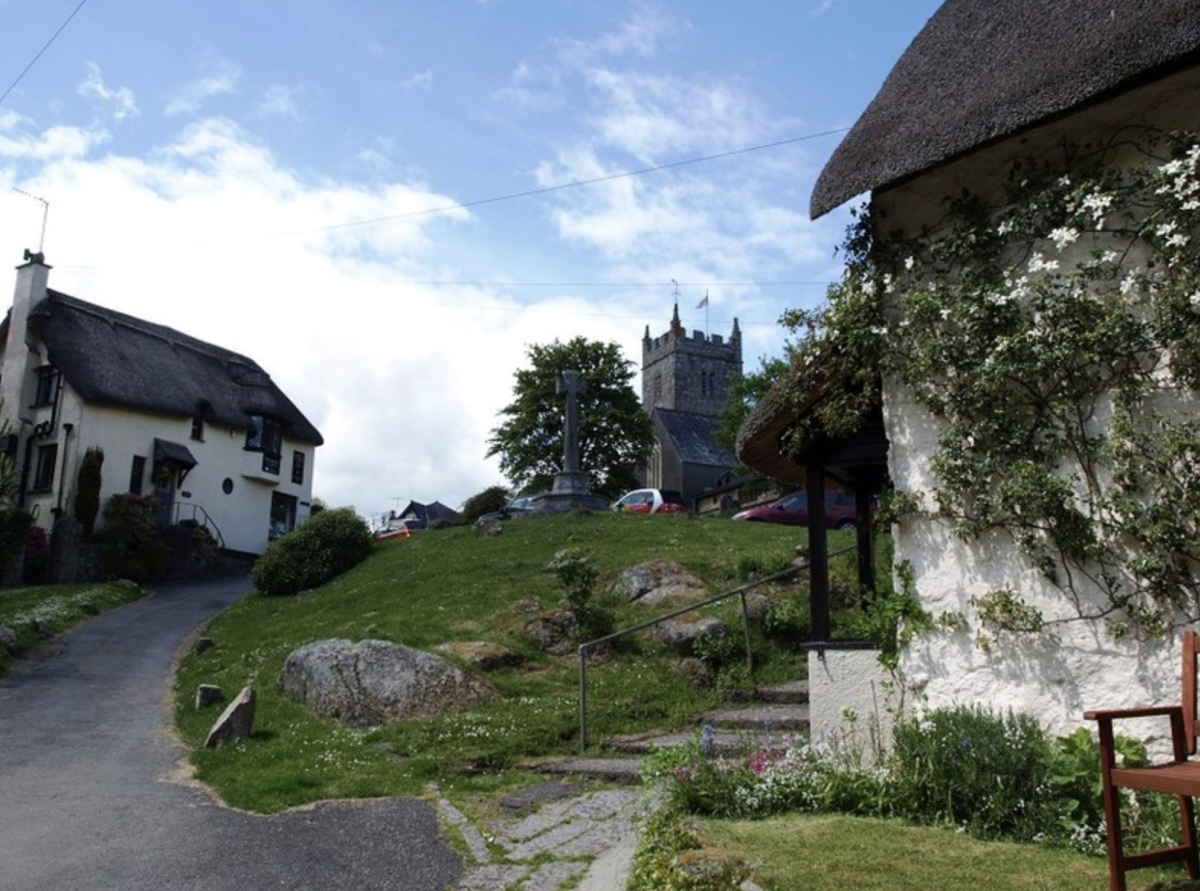 Charming village scene with thatched cottages, a stone church, and lush greenery under a blue sky. Relaxed, idyllic countryside atmosphere.