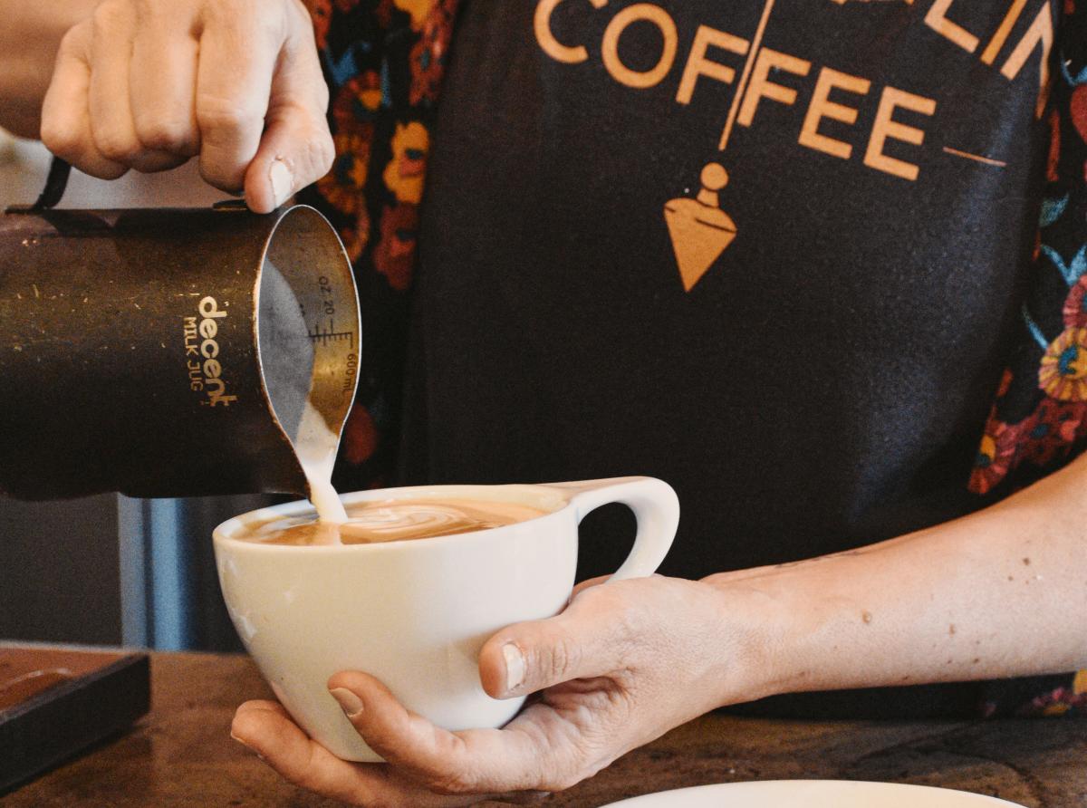 a barista pours coffee into a white mug