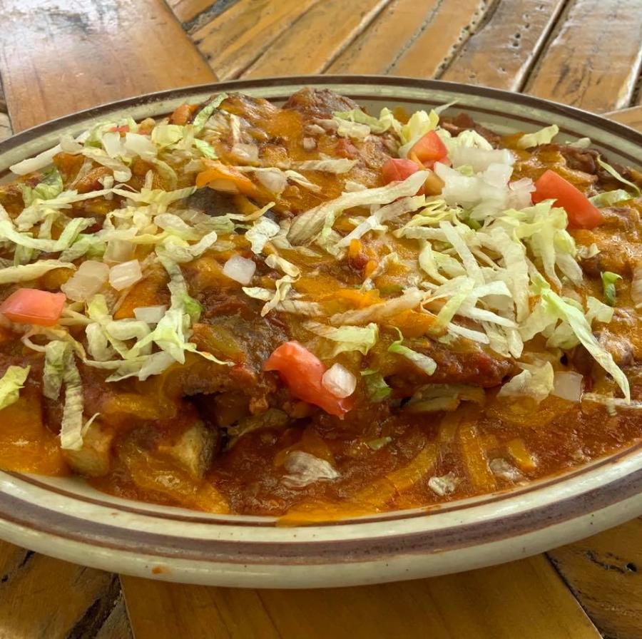 A plate of chile rellenos covered in chile, cheese, lettuce and tomato.