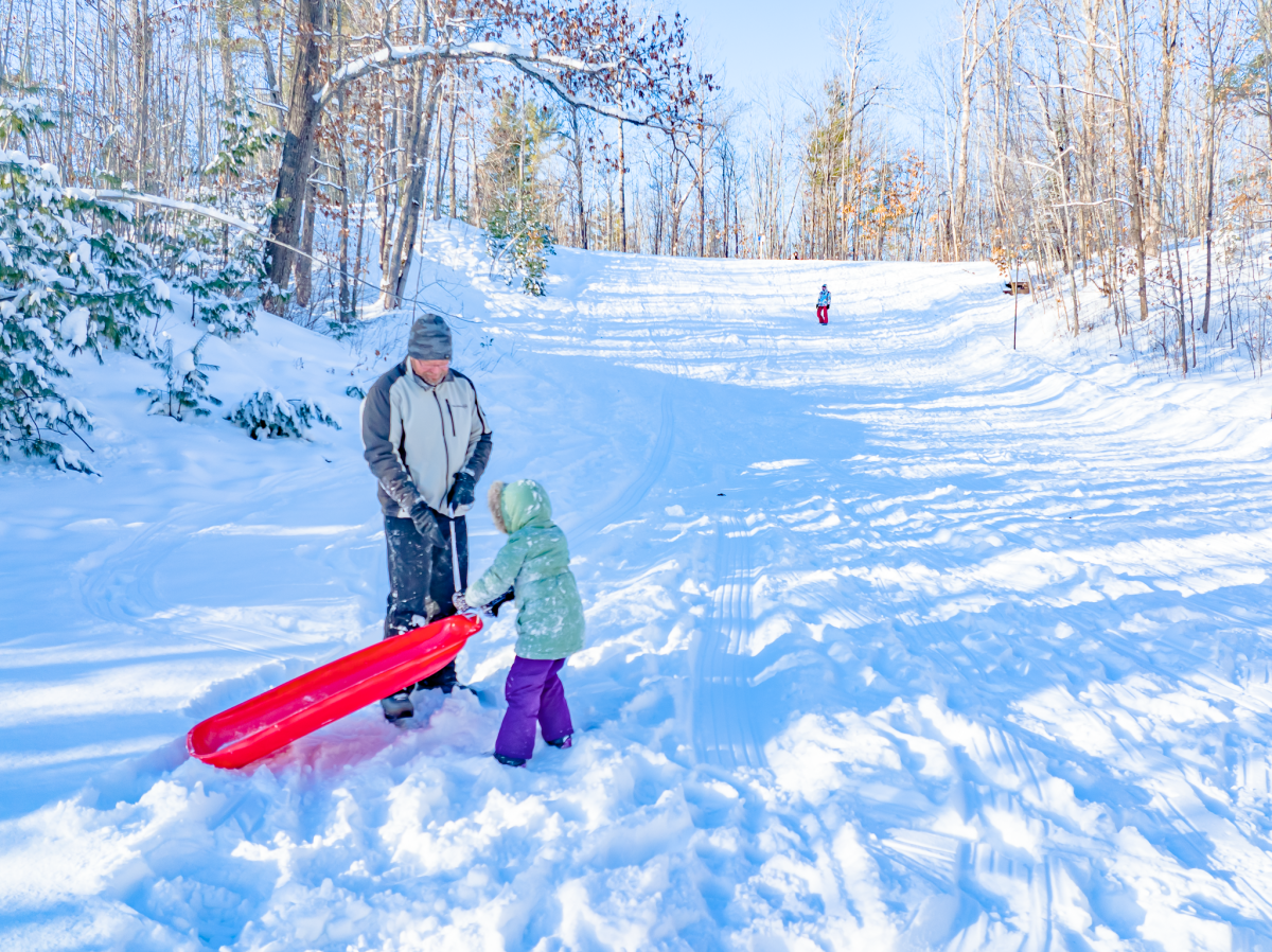 Child and parent pull sled back up hill.