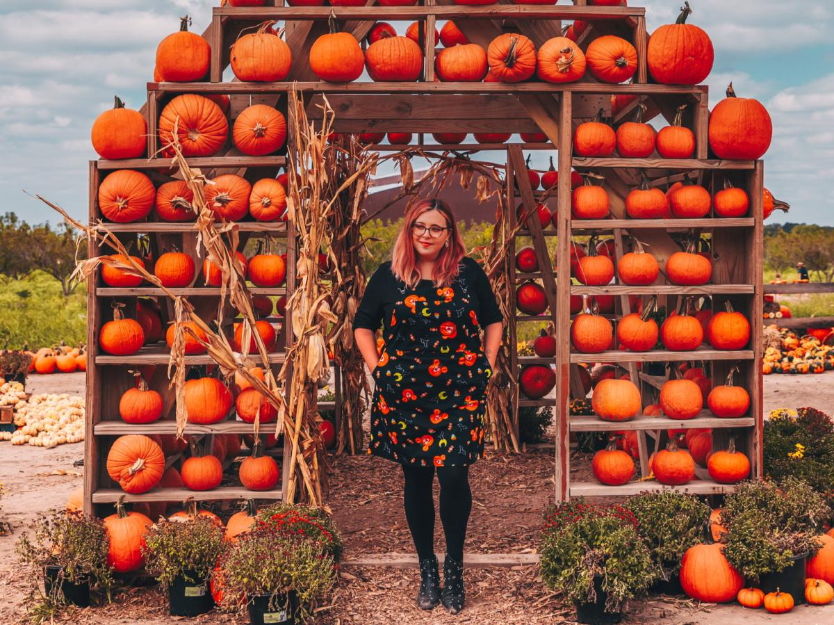 Woman stands in front of a large Fall pumpkin display at Sweet Eats Fruit Farm near Austin Texas