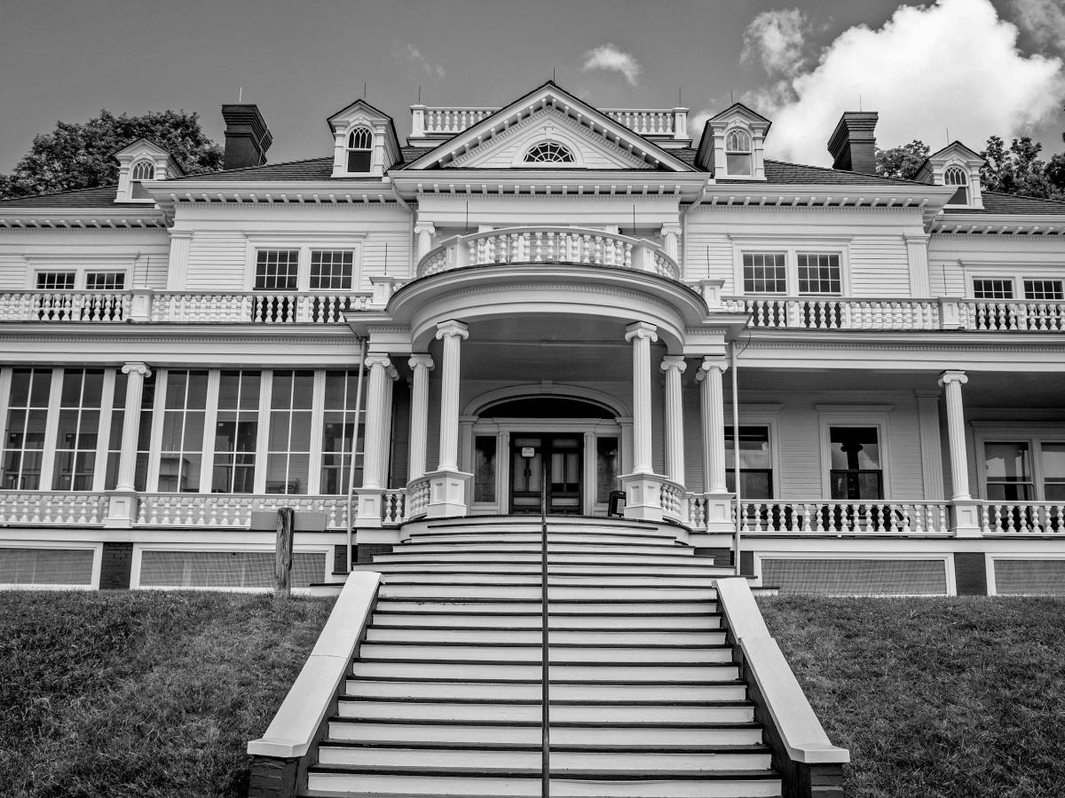 A black and white image of the looming, grand entryway of the stately, white Flat Top Manor at the Moses Cone Estate.