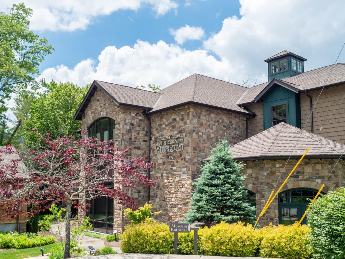 Ornate and colorful trees surround a large bring building, the home of Blowing Rock Art & History Museum.