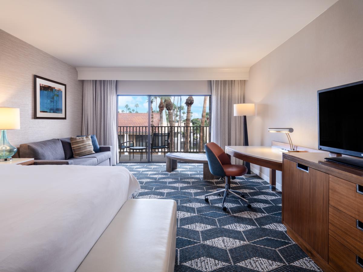 Crowne Plaza Phoenix Chandler hotel room with bed, couch, desk, and dresser with TV and balcony in the background.