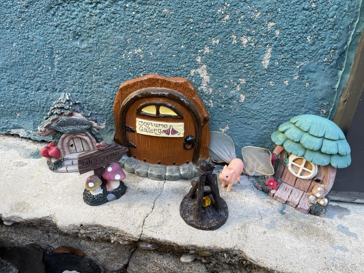 Image of 3 different, tiny, decorative fairy doors on the sidewalk and up against a building.