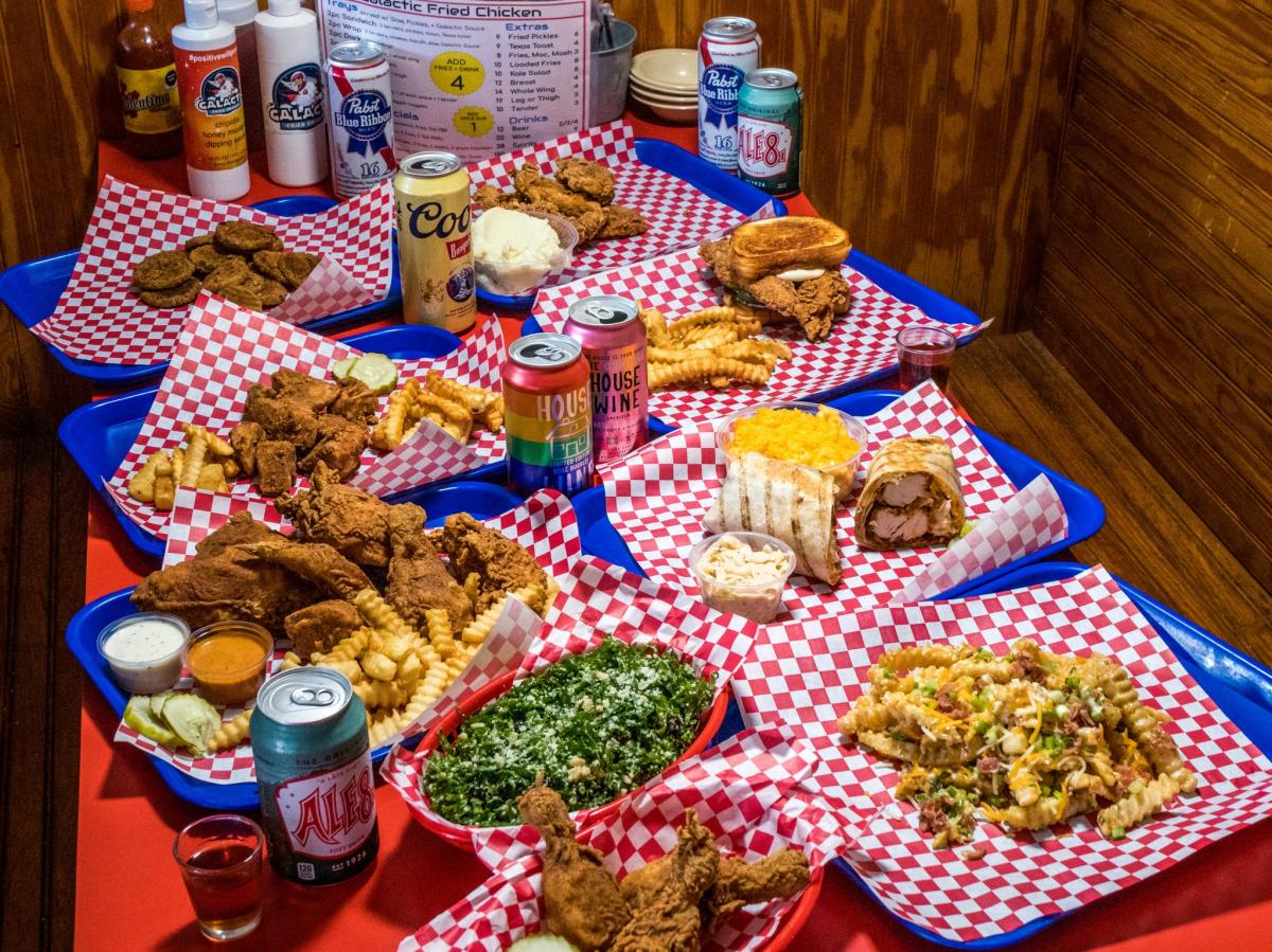 Image is of a table full of different cuisine options including fried chicken, wraps, wings, loaded fried and beverage options.