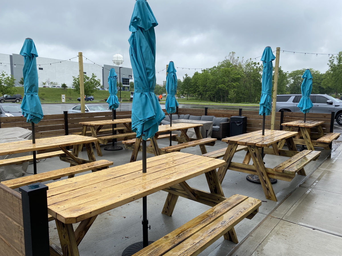 Image is of an outdoor patio featuring a number of wood, picnic tables with umbrellas.