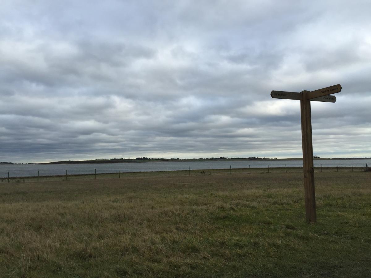 Signs at Abberton Reservoir against a cloudy sky.
