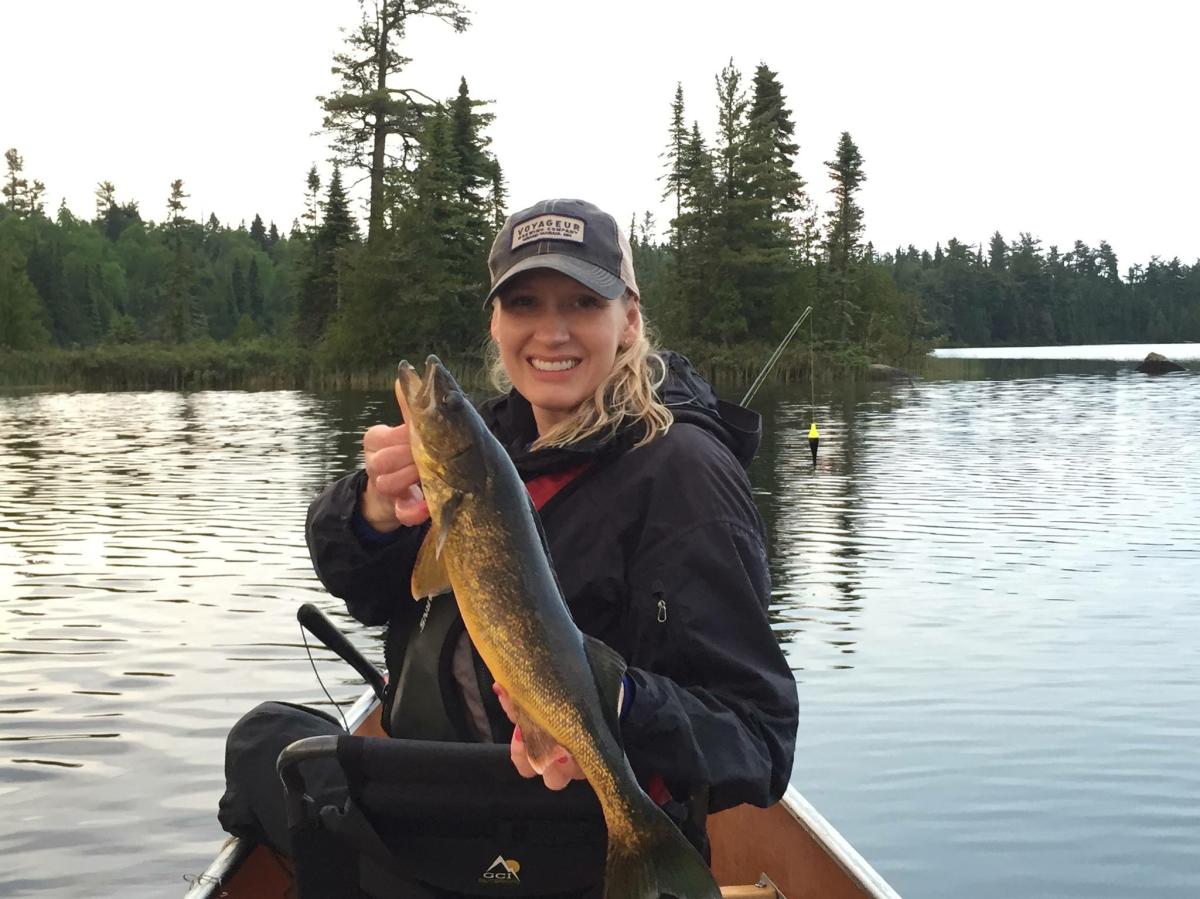 A woman holding a walleye in a canoe.