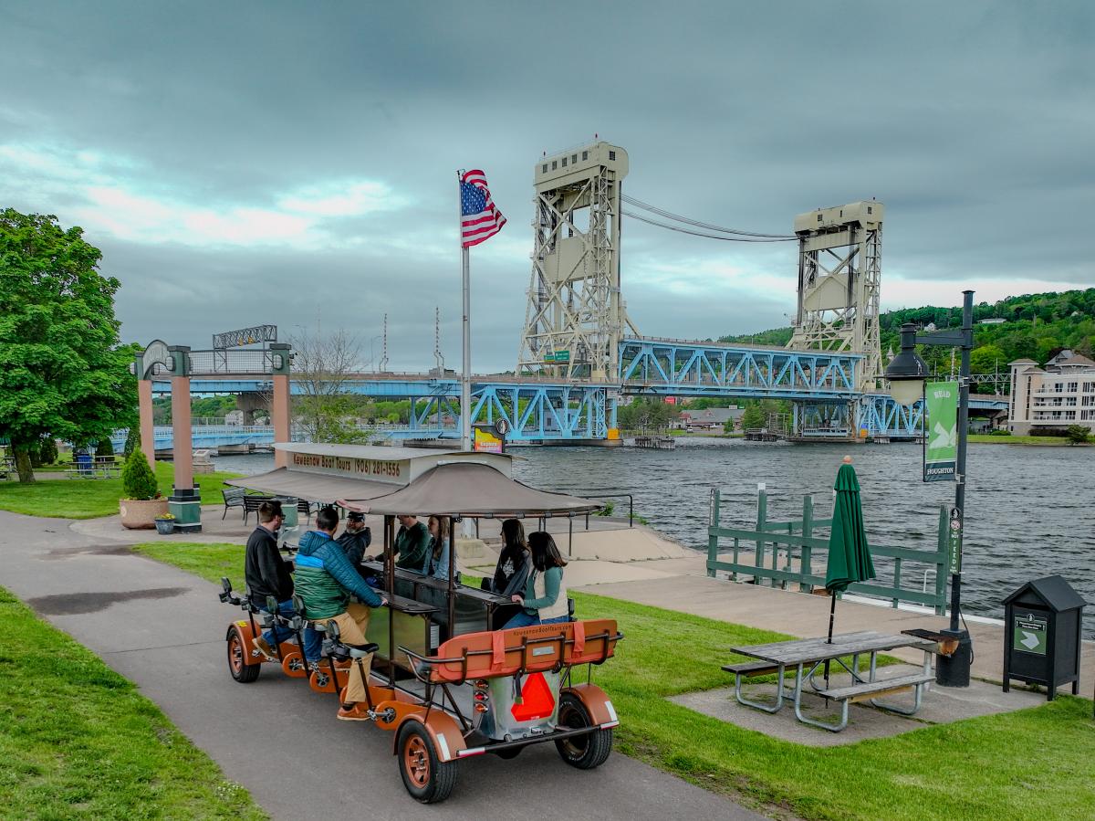 a pedal trolley car rides the sidewalk in front of the Portage Lake Lift Bridge
