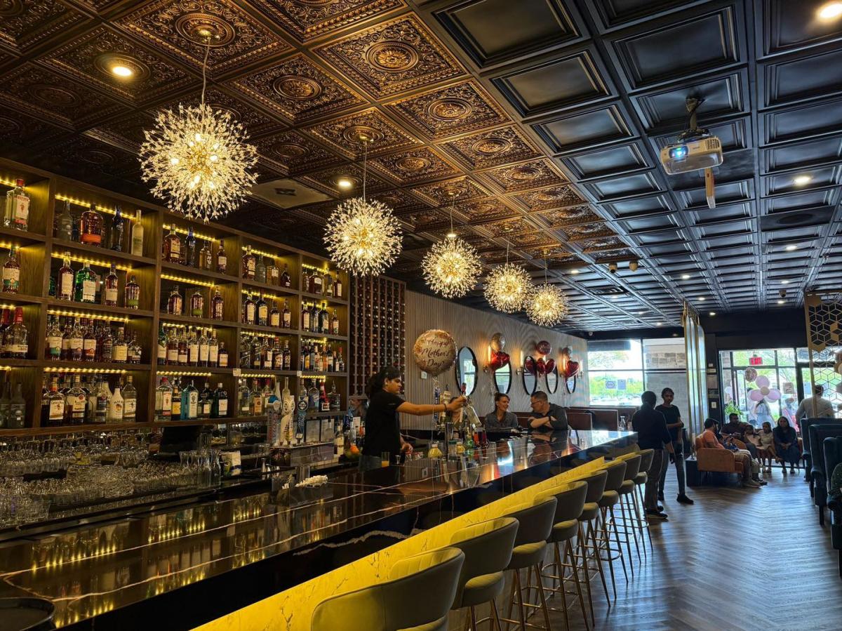 Bartender at the marble bar inside Biryani Grill in Ashburn, Virginia with starburst chandeliers and a backlit wall of spirits