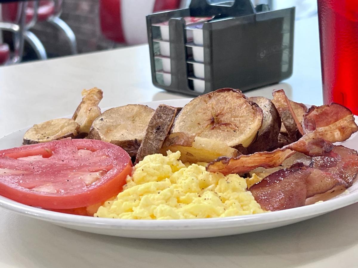 plate of scrambled eggs, bacon, potatoes and tomato slice.