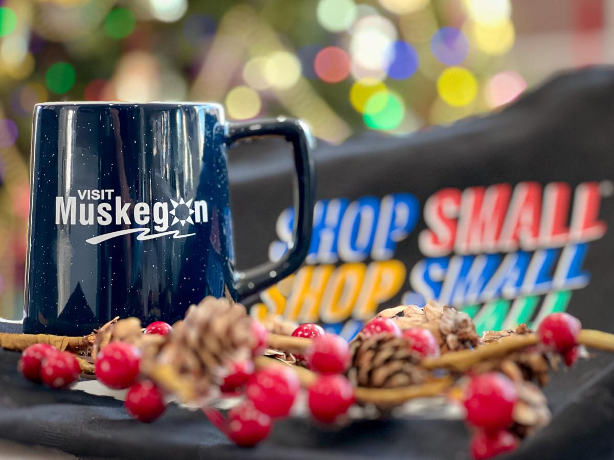 Blue mug with white Visit Muskegon log sits among holiday decor and Shop Small shopping bag