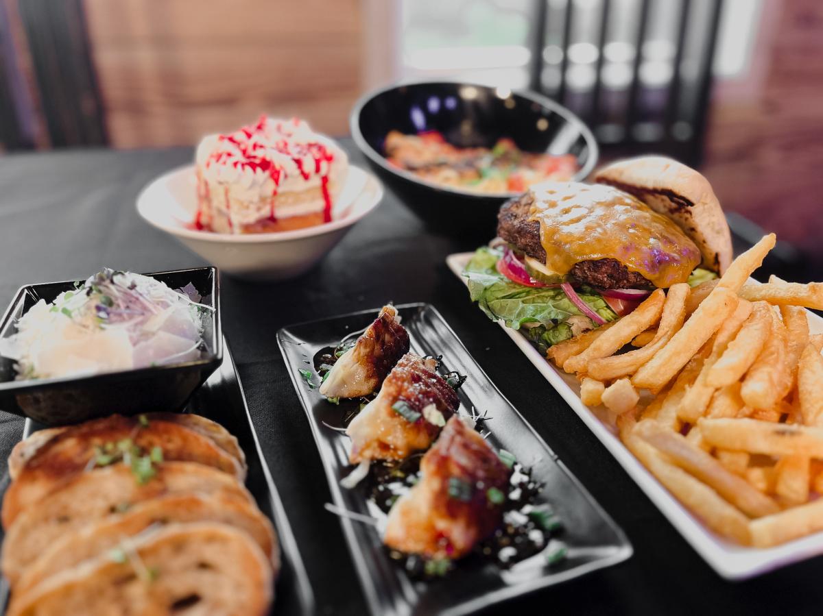 Table of food including a burger and fries, potstickers, chicken alfredo, bruschetta and dip, and strawberry shortcake