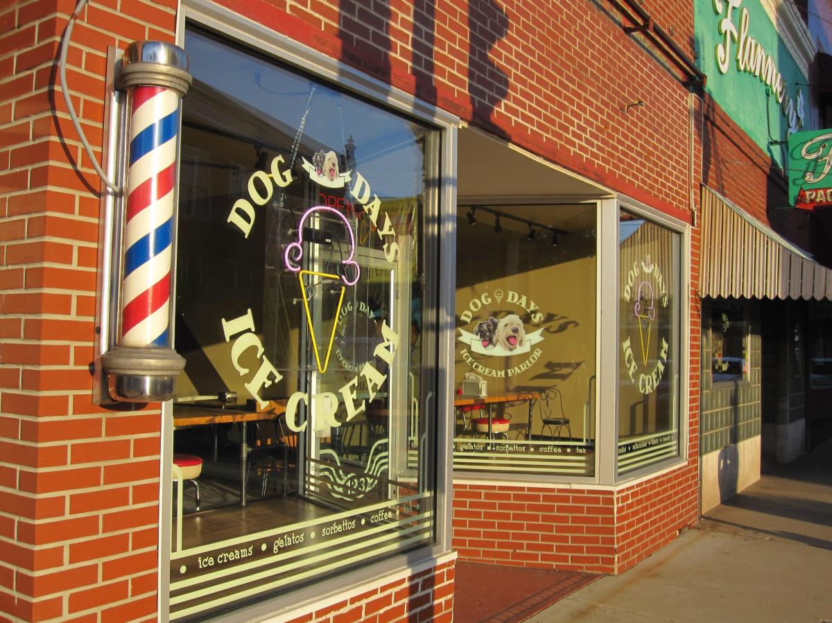 A storefront with red brick and glass windows. The window has a logo with an ice cream cone and "Dog Days Ice Cream"