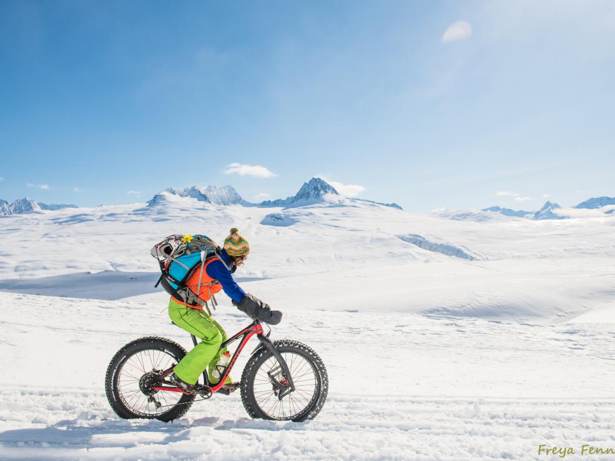 a fat biker in bright colors riding in a winter mountain pass