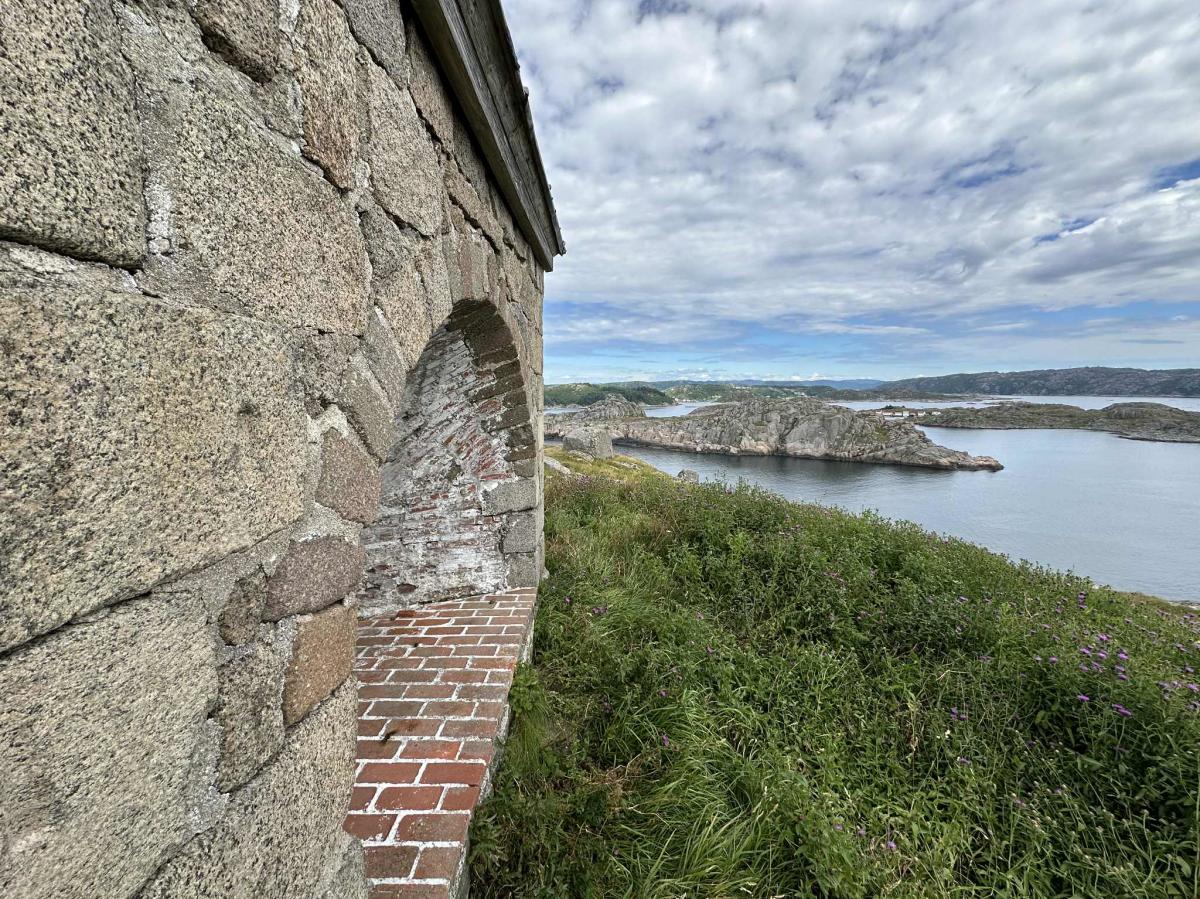 Nærbilde av steinveggen på Markøy fyr, med utsikt mot kystlandskapet og havet i bakgrunnen.