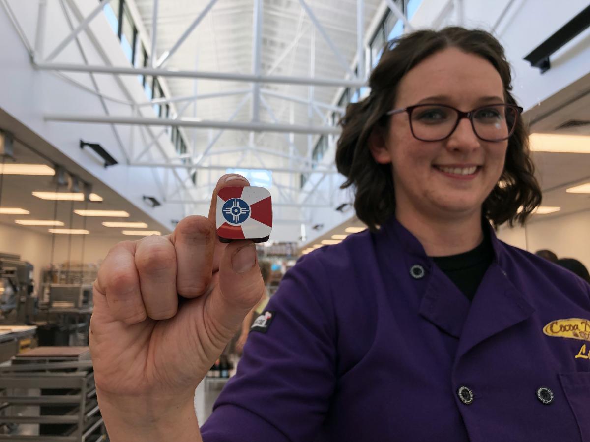 A Cocoa Dolce employee holds up a piece of chocolate printed with a Wichita flag design
