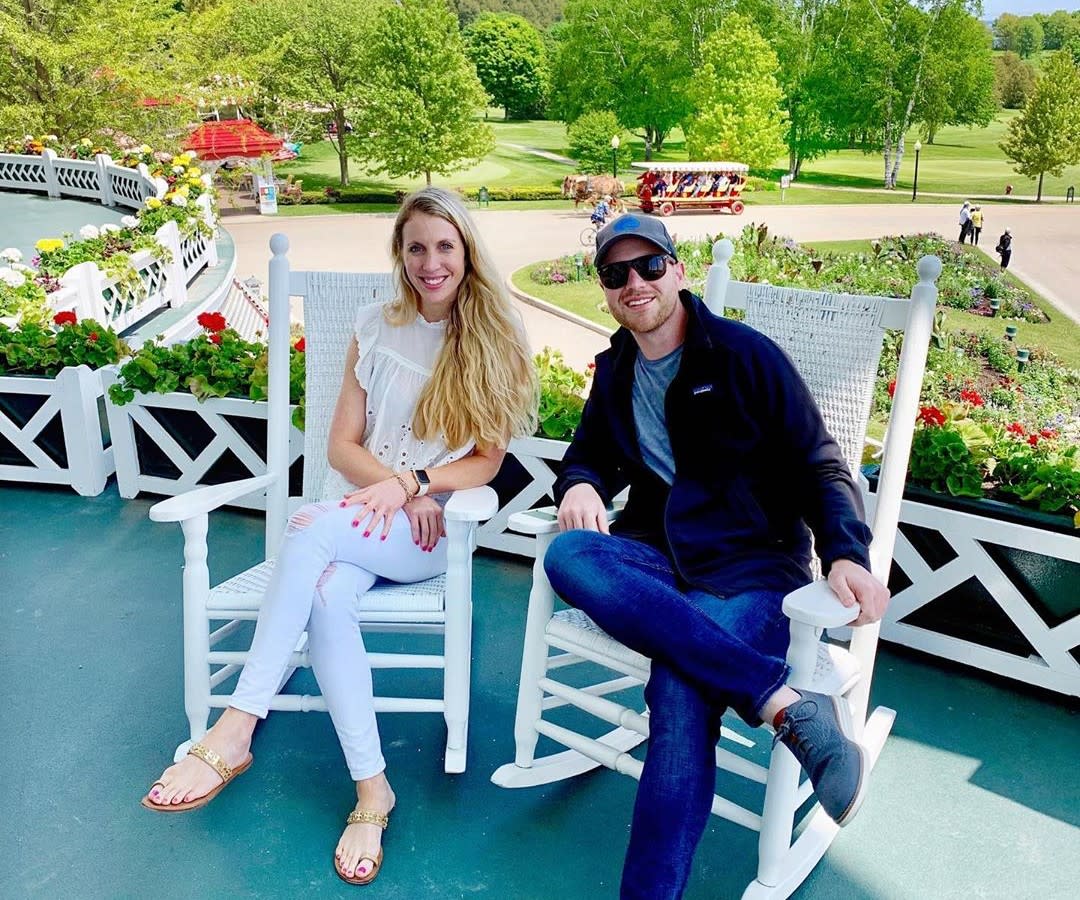 Young couple sitting in rocking chairs on a Mackinac Island porch with horse-drawn carriage and golf course in background