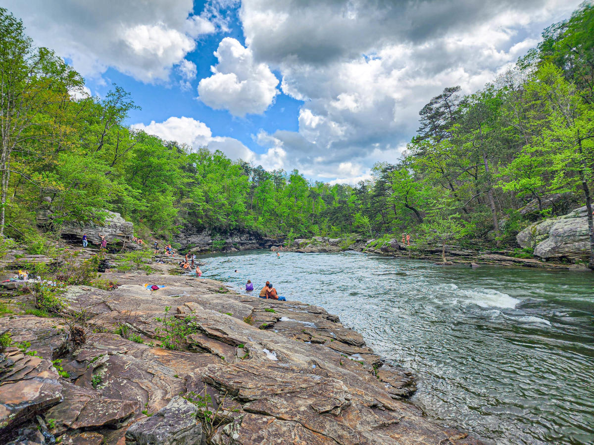 People enjoying the Hippie Hole at Little River Canyon with rocks and green trees.