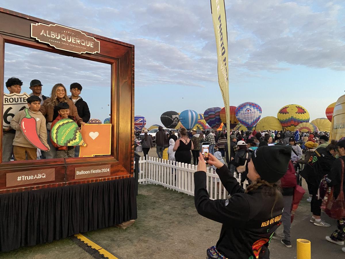 A Visit Albuquerque employee takes a picture of a family in the Visit Albuquerque frame at Balloon Fiesta.