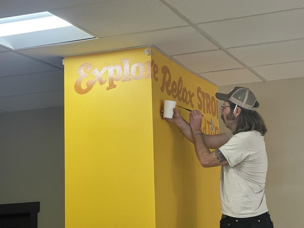 A photo of Chad Lindsay painting words onto the columns at the Route 66 Downtown Information Station.