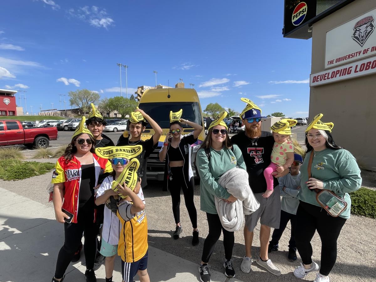 A large group of people poses in front of the Visit Albuquerque van. Everyone is wearing a Banana hat that Visit Albuquerque made.