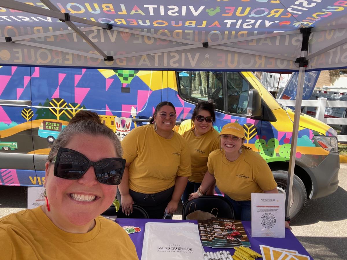 Four Visit Albuquerque employees pose in front of the Visit ABQ van at the 2024 New Mexico State Fair.
