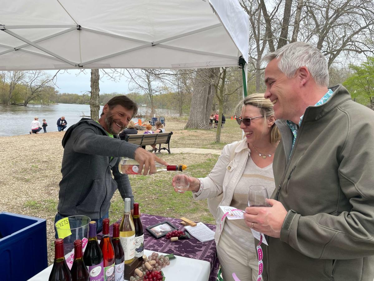A couple is served wine from a booth at Wine on the Fox with the Fox River in the background