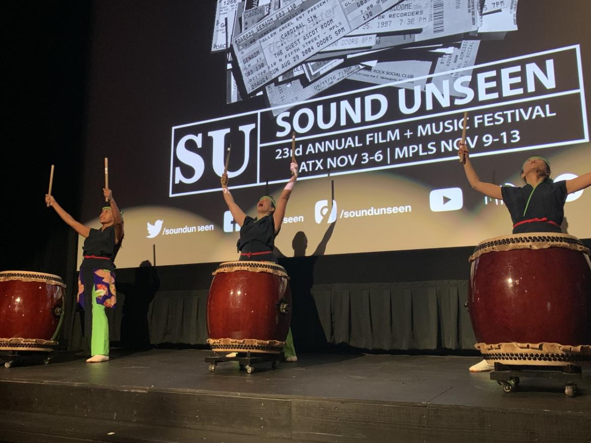 Image of three individuals beating three large drums onstage at Sound Unseen film festival.