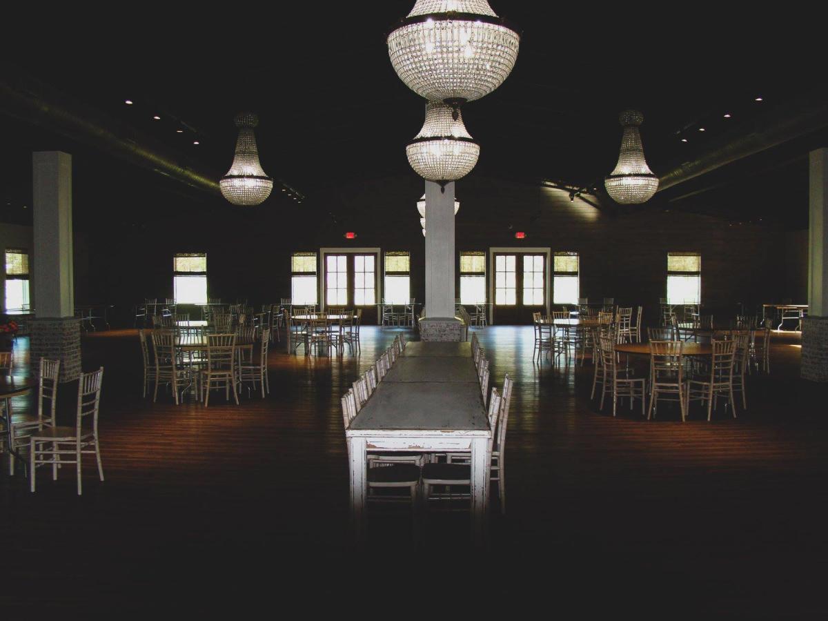 The reception space of Venue at Belle Oaks has hardwood floors and elegant chandeliers.