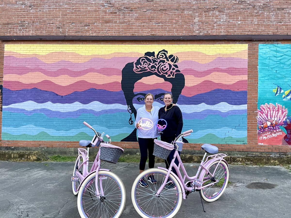 Two Woman With spindletop cruisers bikes In front Of A Frida Mural