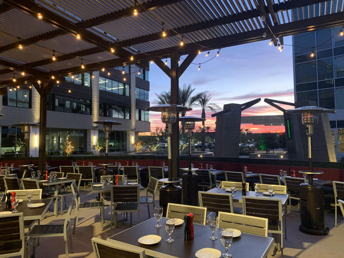 Patio at sunset at The Sicilian Butcher. Tables and chairs with table setting and garden lights on.