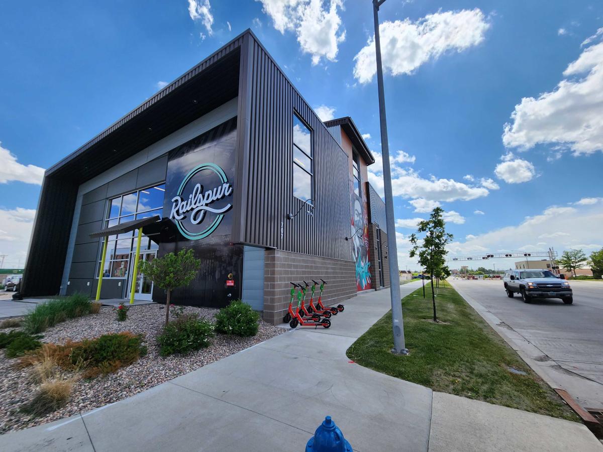 Modern architecture of The Railspur building in Cheyenne, featuring a large logo and vibrant mural on a sunny day.