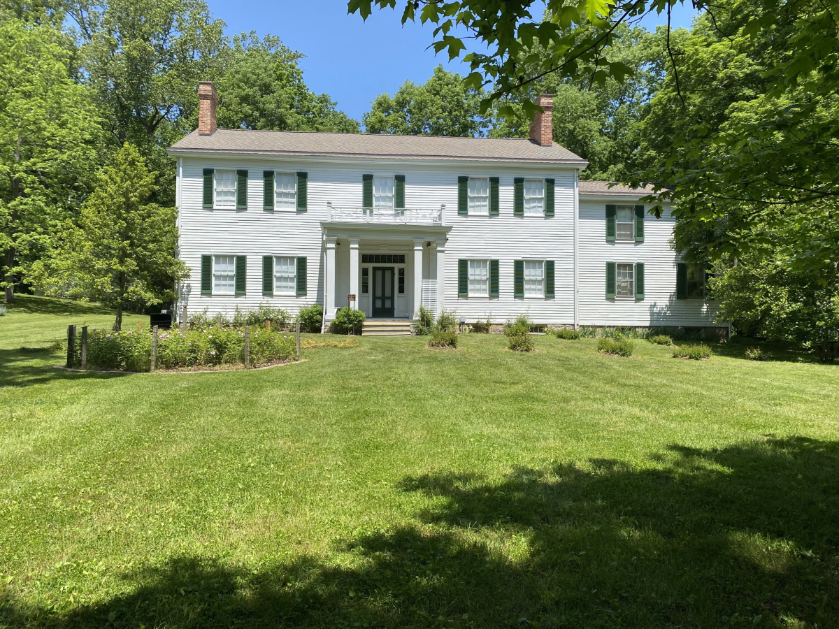 Image is of the Dinsmore Homestead house during the summer with trees in bloom on a bright and sunny day.