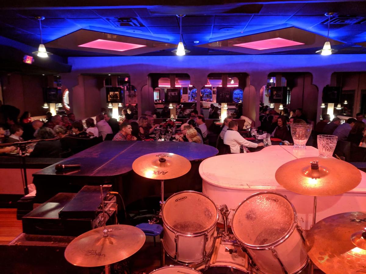 Image is of inside the bar with two pianos' next to each other and people sitting at tables in the back ground.