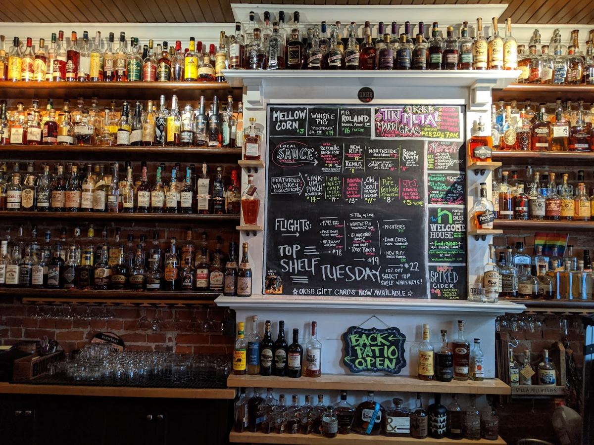 A wall covered in bottles of bourbon with a chalkboard menu at the center at OKBB