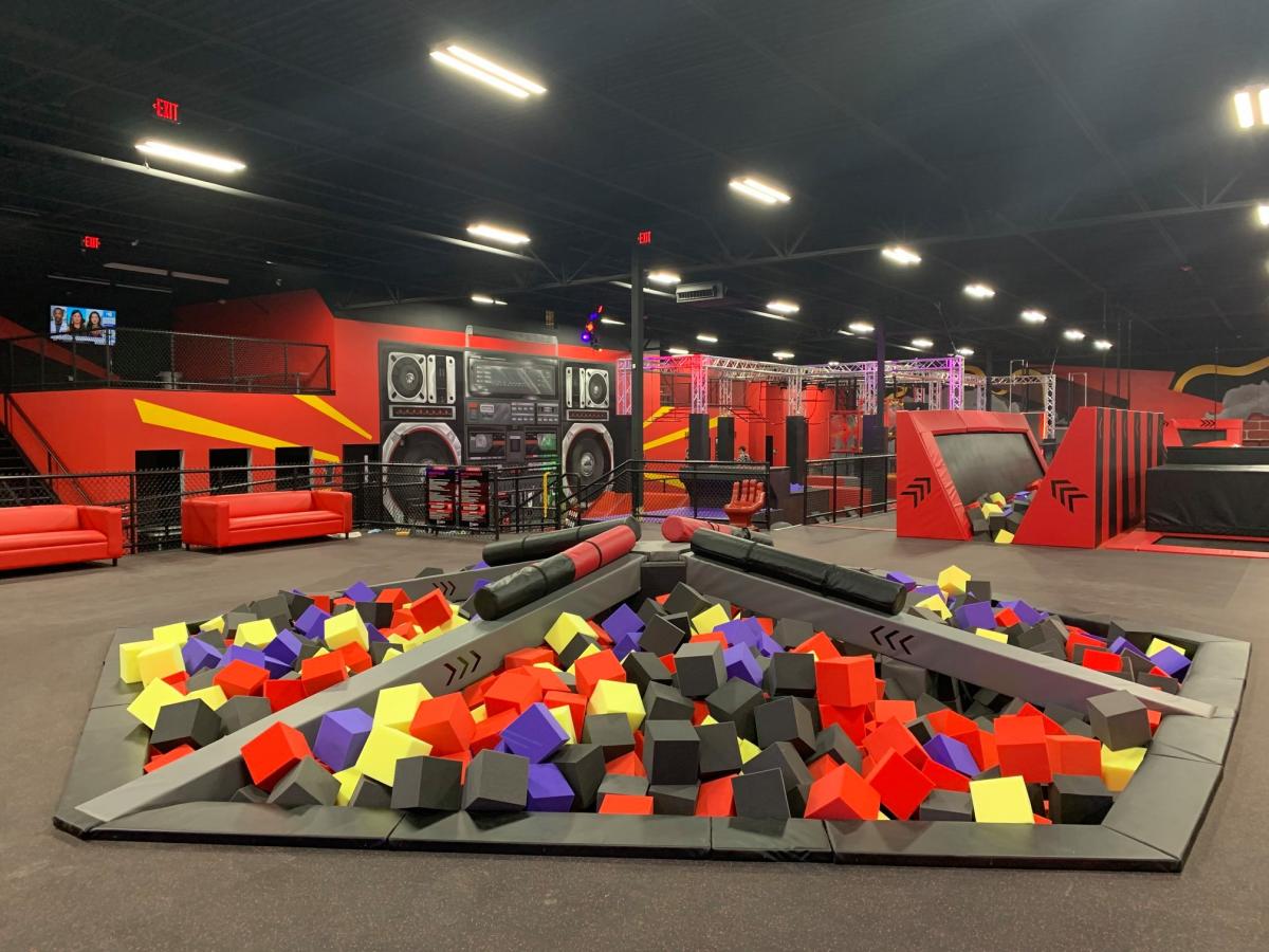 Black floor with red walls in the background. The room is filled with pits full of foam squares in black, red, yellow and purple