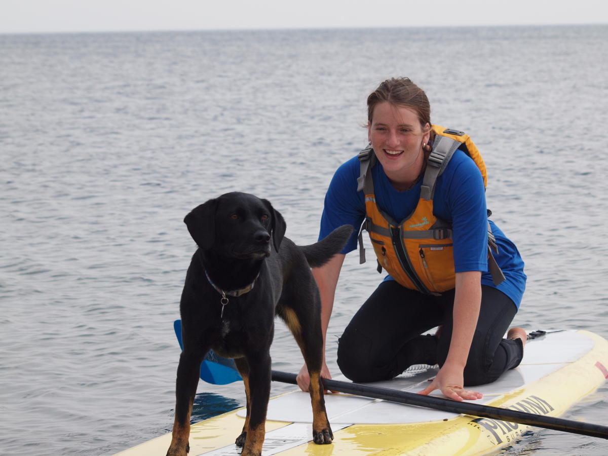 A woman on a paddle board with her dog also on the board