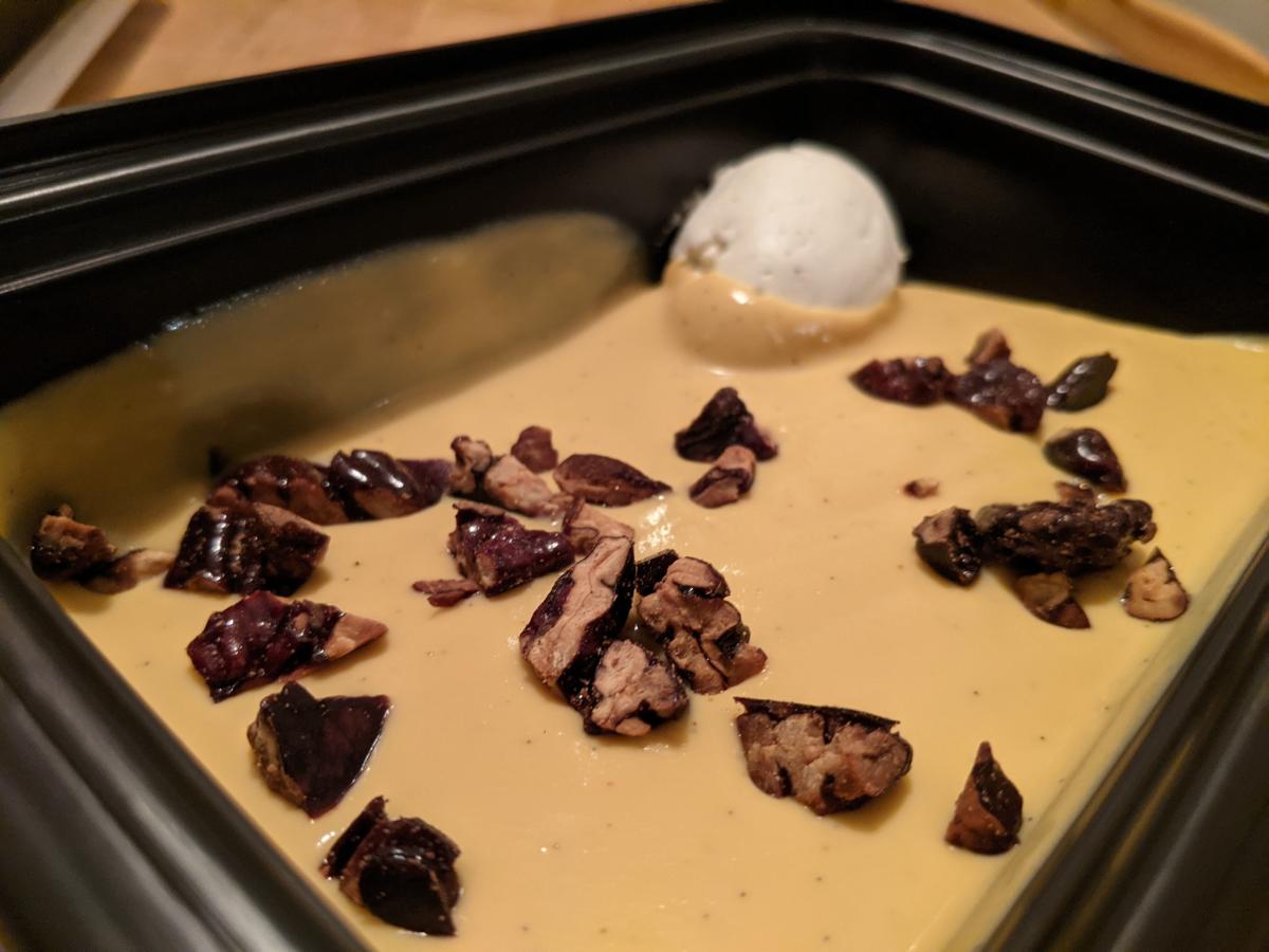 Butterscotch Pudding in a takeout container from Bolete is topped with candied pecans and fresh whipped cream.