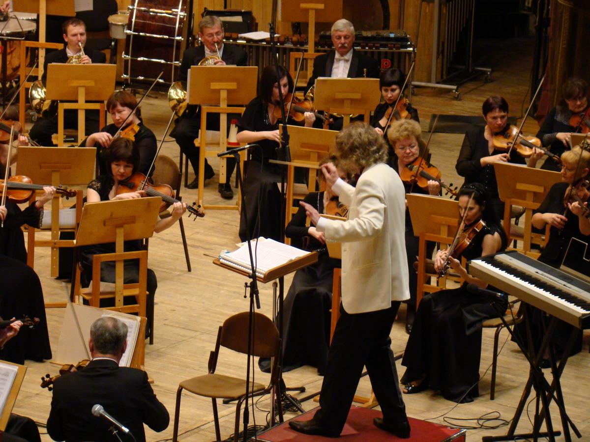 An orchestra is playing while a conductor in a white coat is directing their tempo.