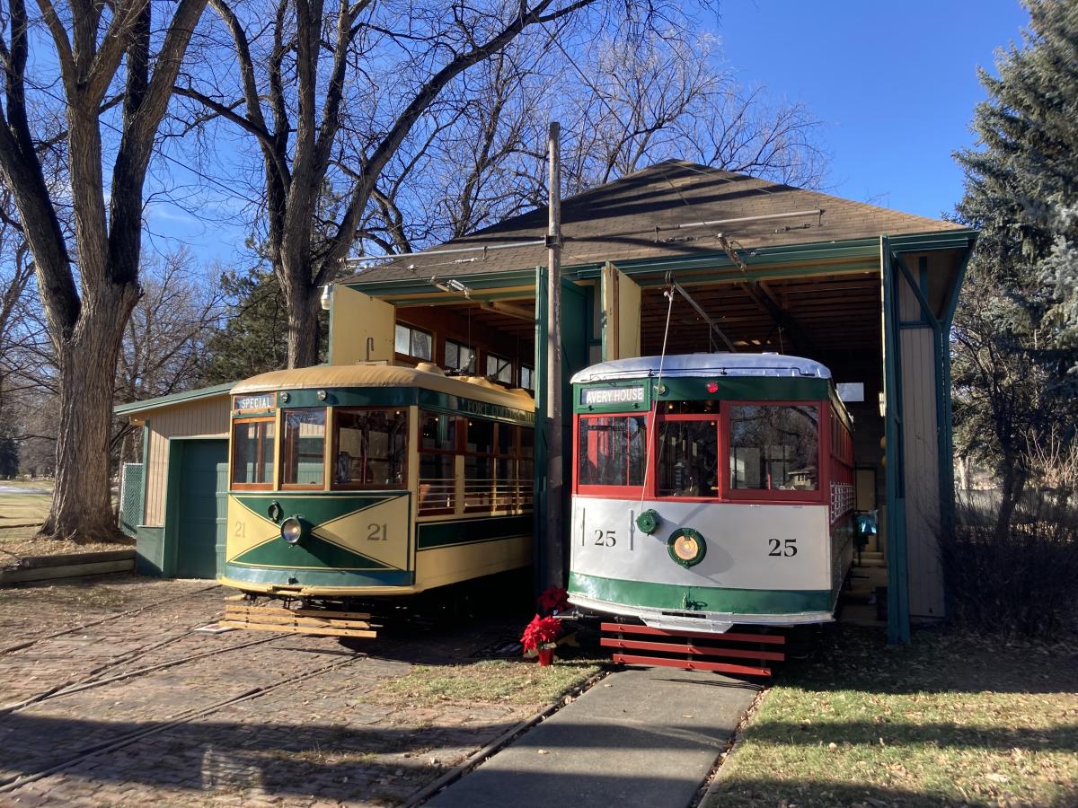 Two trolleys, one red and white and green and one yellow and green next to each other at the trolley barn